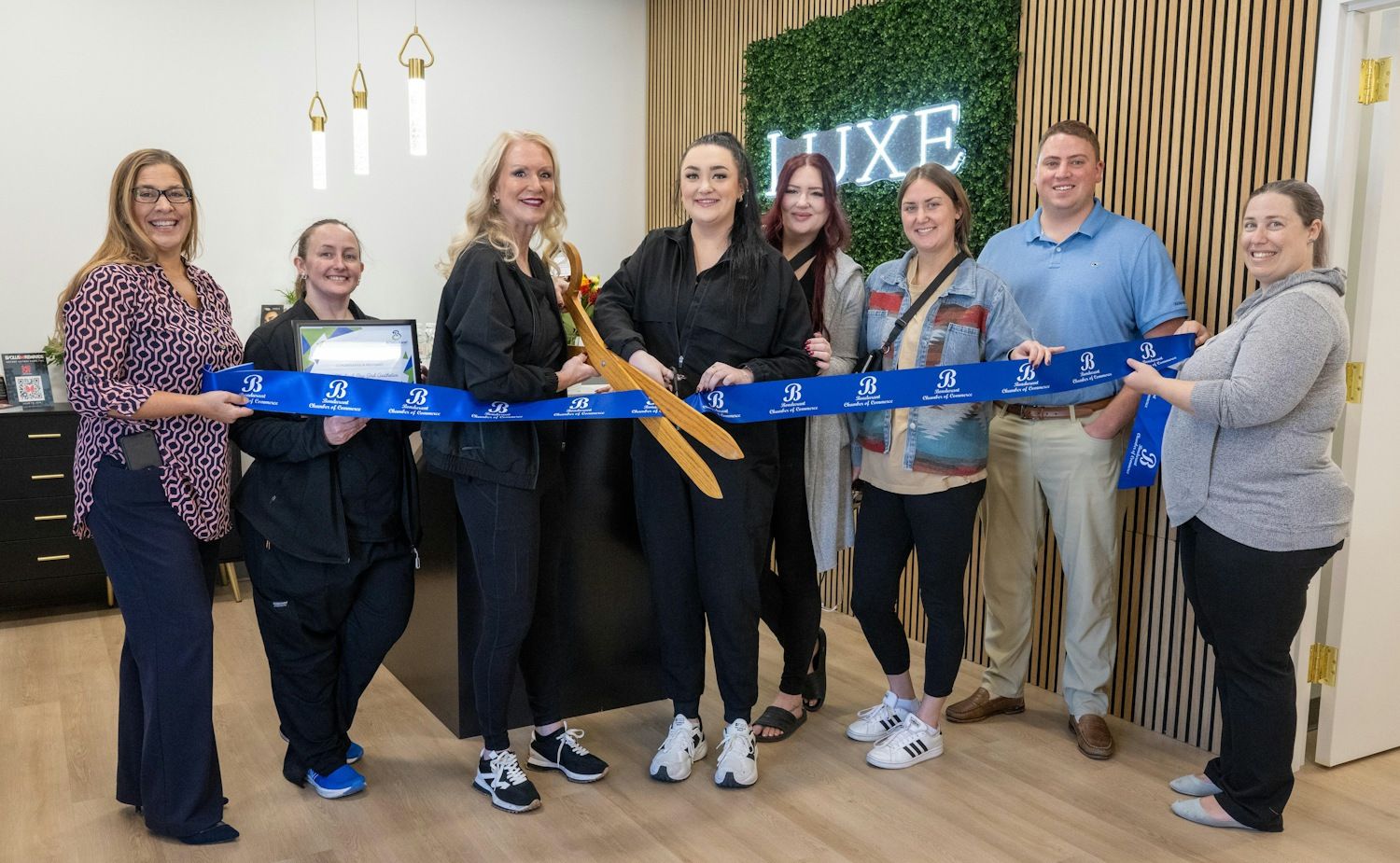 Luxe business and Bondurant Chamber of Commerce members holding a ribbon with oversized scissors ready to cut the ribbon